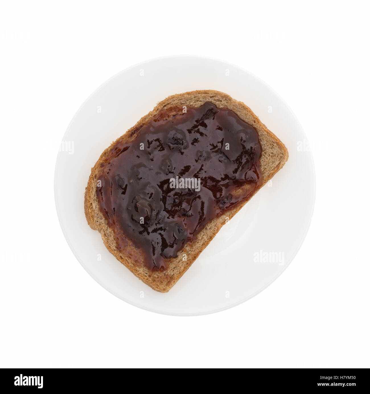 Top view of plum preserves spread on a piece of wheat bread on a plate isolated on a white background. Stock Photo