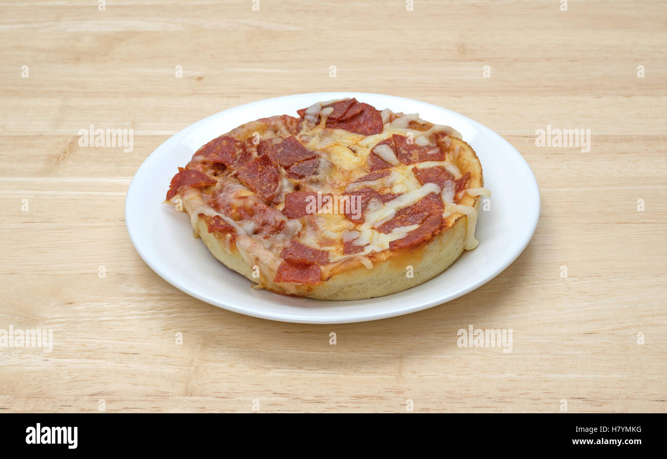 A microwaved personal size pepperoni pizza isolated on a white plate