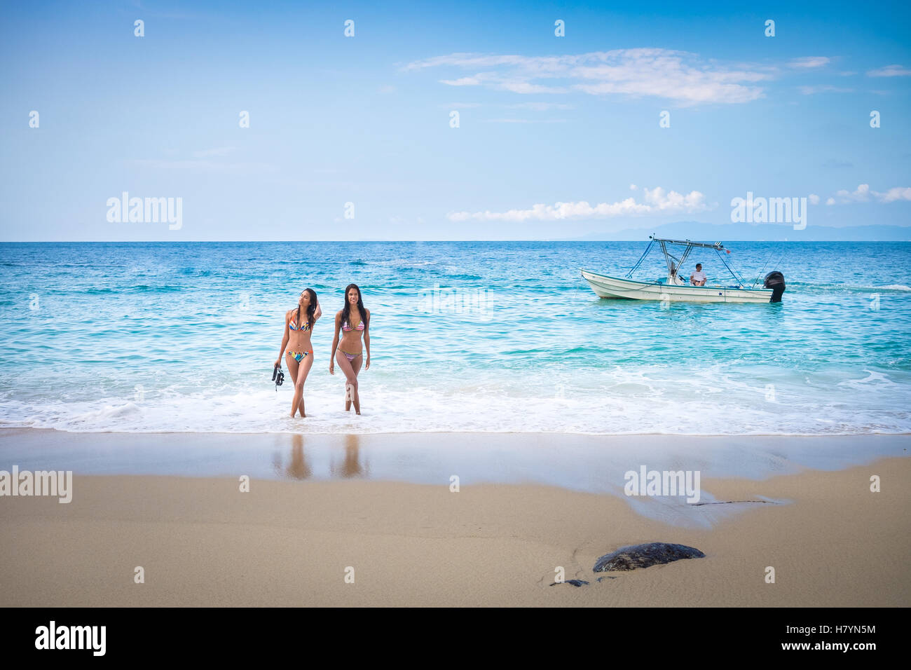 Beach scene with two attractive latina women stepping out of the ocean. Fishing boat in the background. Banderas Bay - Pacific O Stock Photo