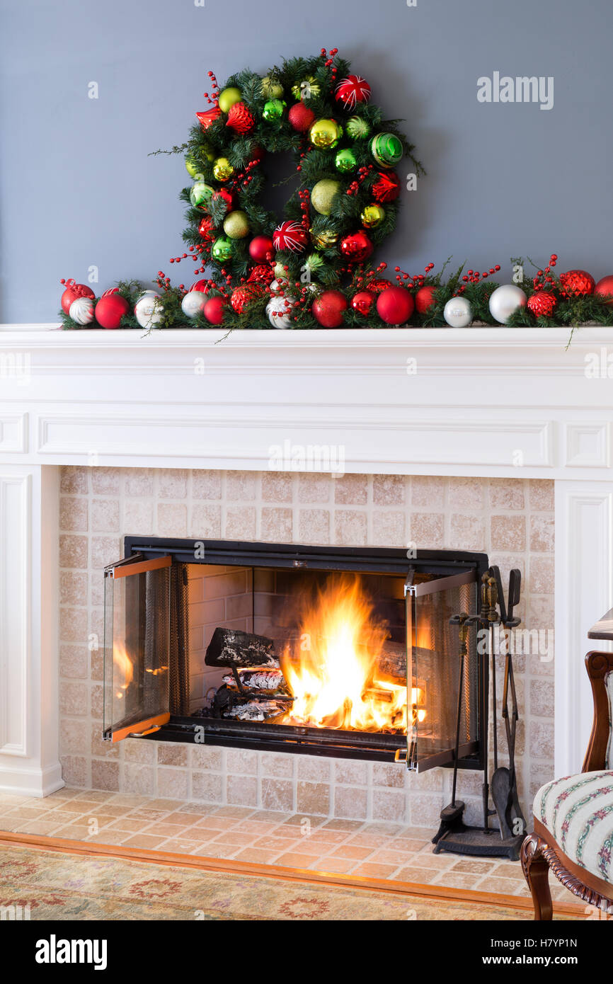 Christmas fireplace with colorful decorations and and a traditional Xmas wreath above a blazing fire in the hearth for a warm co Stock Photo