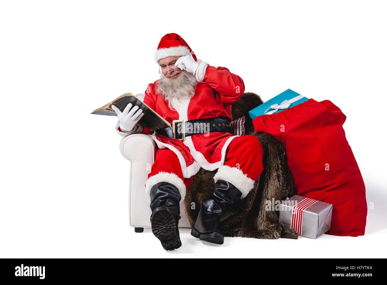 Santa reading bible with sack of christmas present beside him Stock Photo