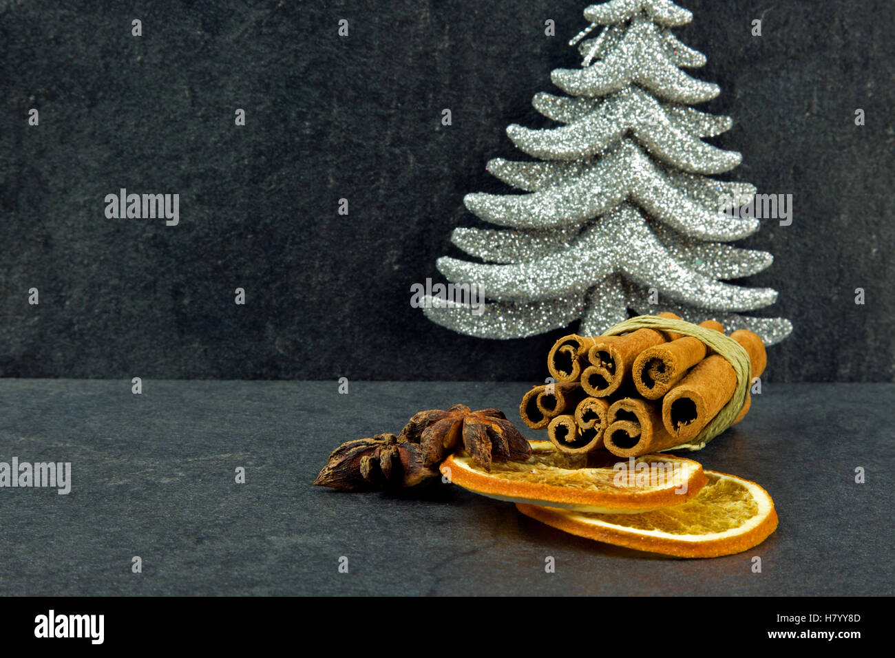 Cinnamon sticks, star anise, two slices dried orange and silver Christmas tree on a dark, stone table with shallow depth of fiel Stock Photo