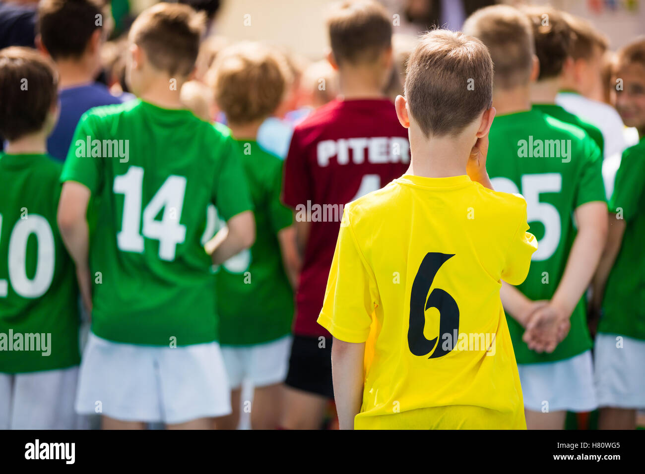 Young boy in yellow sport uniform with player number on the back standing alone. Young sports