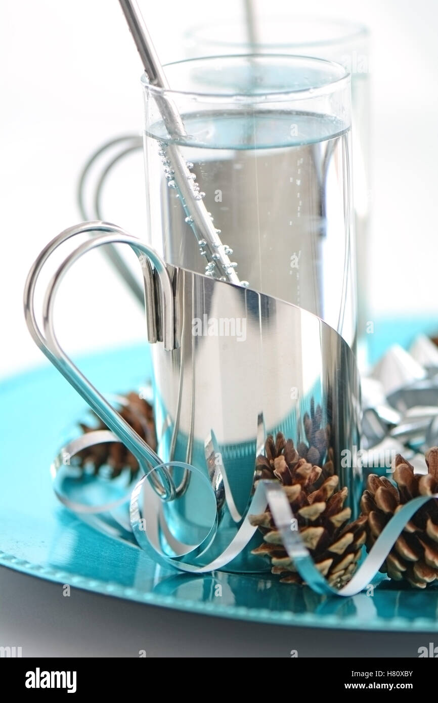 Sparkling non-caffeinated, soft drink in silver holder on turquoise tray with festive pine cones and silver ribbon curls Stock Photo