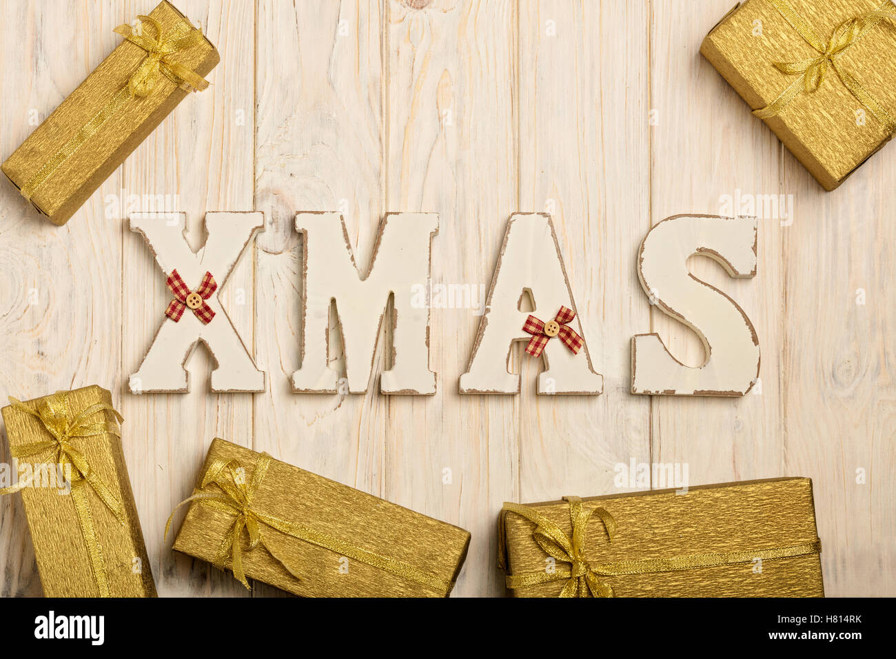 Wooden white XMAS letters on a white wooden background with gifts, Packed in gold paper. Stock Photo
