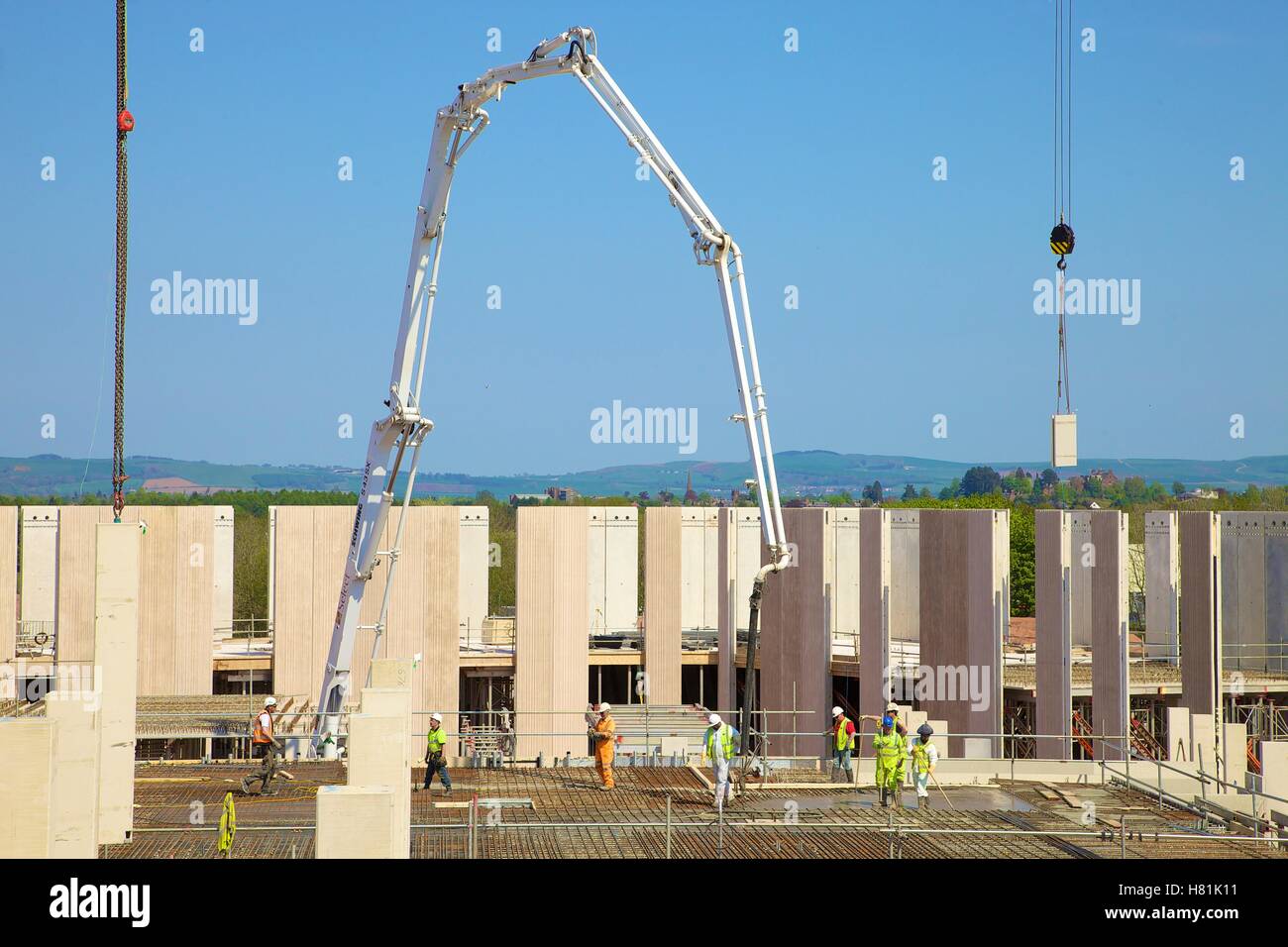Boom concrete pump pouring concrete on to rebar at a construction site. Workers wearing safety clothing on the building site. Stock Photo