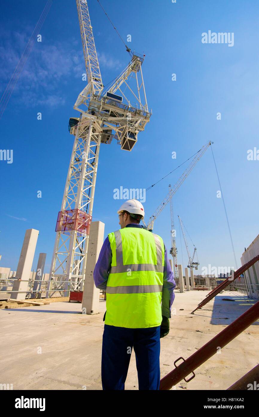 Worker wearing safety clothing watching construction using tower cranes. Stock Photo
