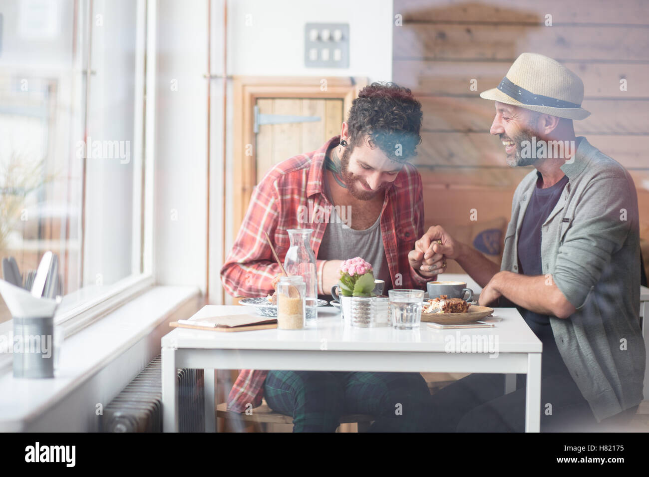 Gay couple sat holding hands in cafe Stock Photo