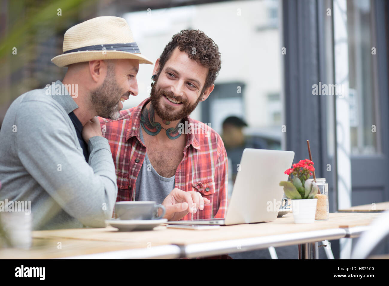 Gay couple sat sharing laptop in cafe Stock Photo