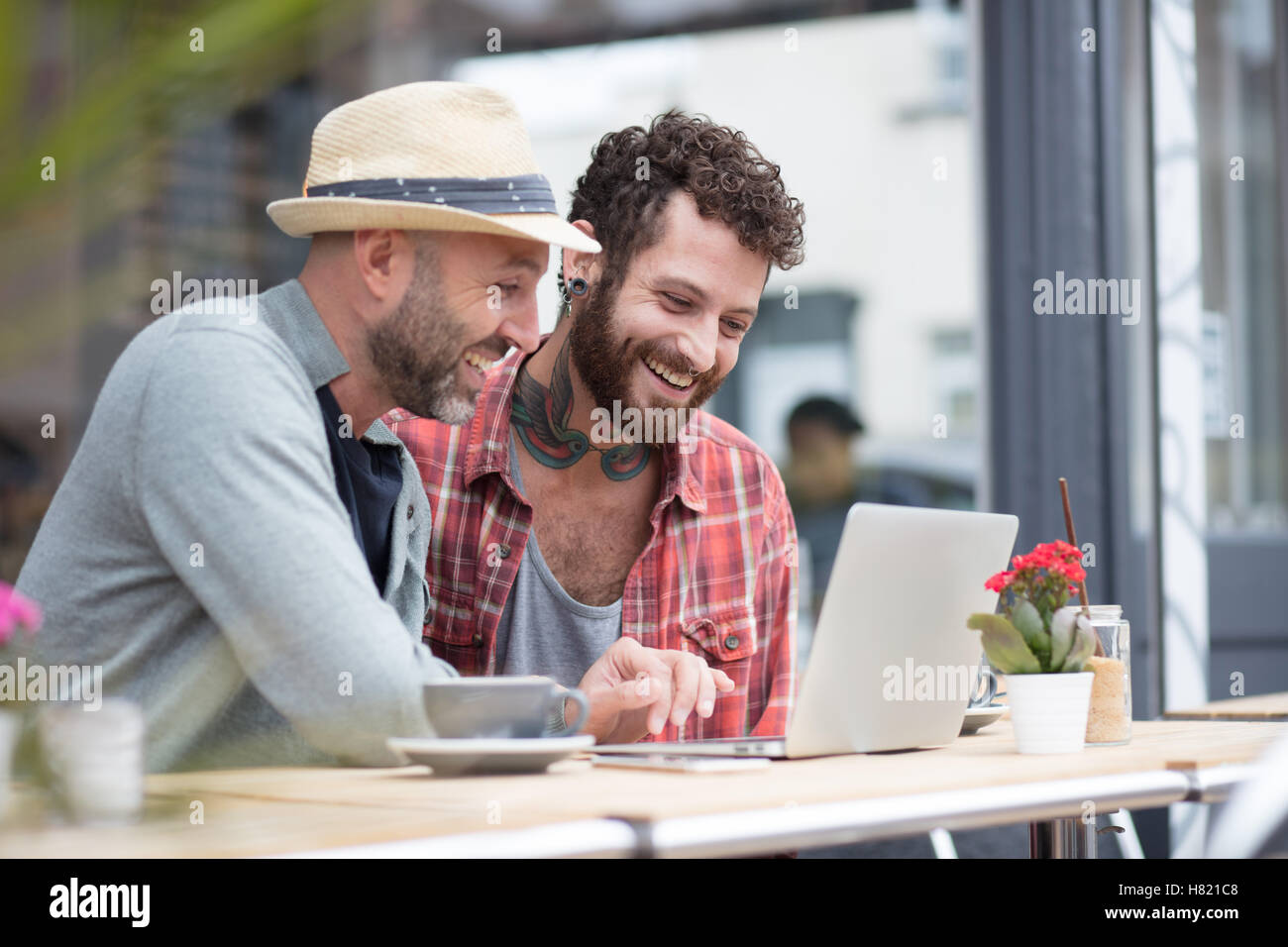 Gay couple sat sharing laptop in cafe Stock Photo