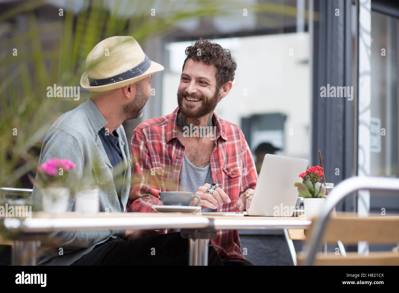 Gay couple sat sharing laptop in cafe Stock Photo
