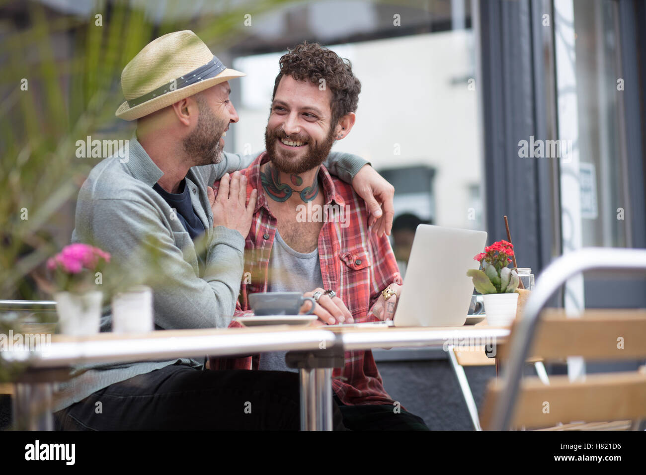 Gay couple sat sharing laptop in cafe Stock Photo