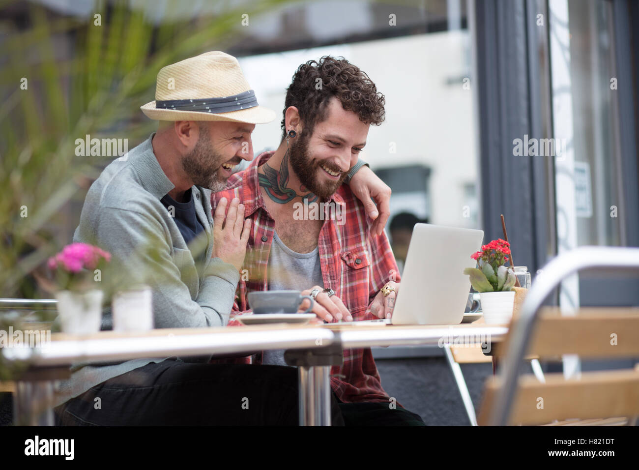 Gay couple sat sharing laptop in cafe Stock Photo
