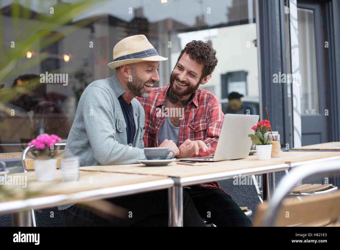 Gay couple sat sharing laptop in cafe Stock Photo