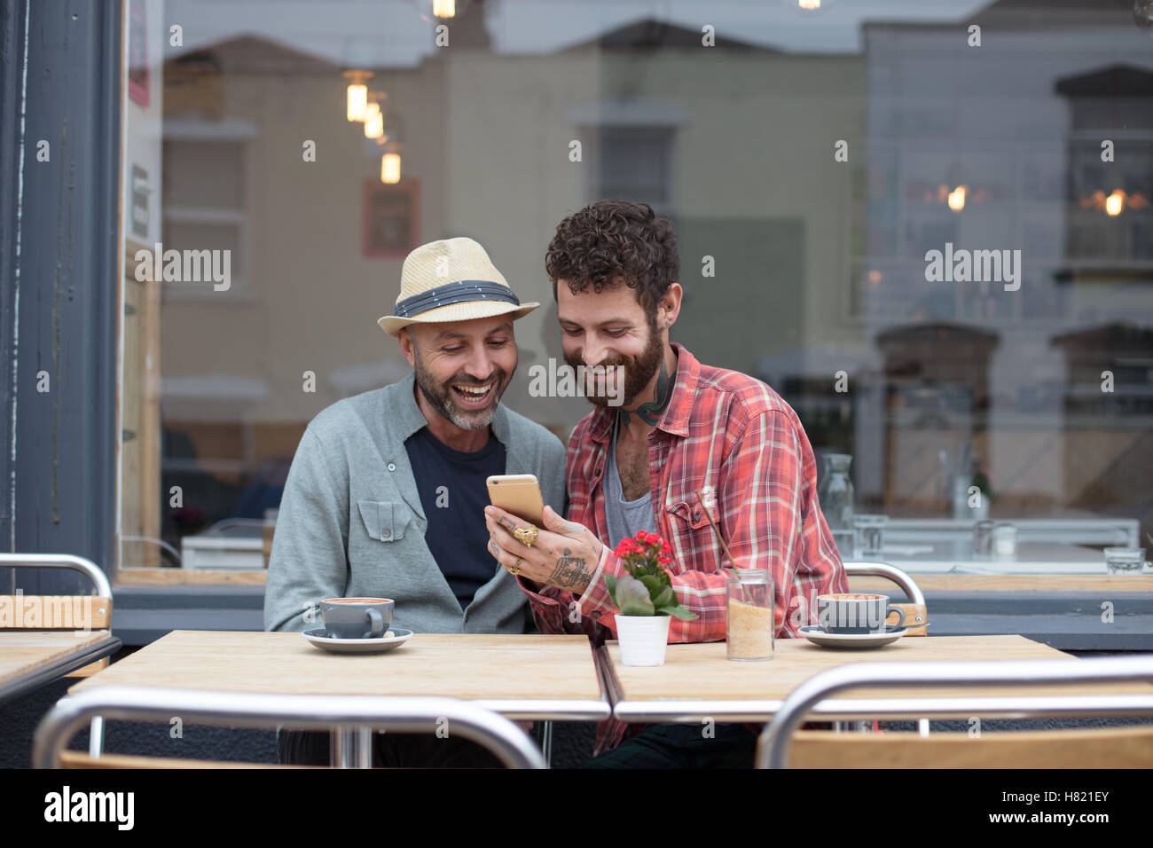 Gay couple sat sharing phone in cafe Stock Photo
