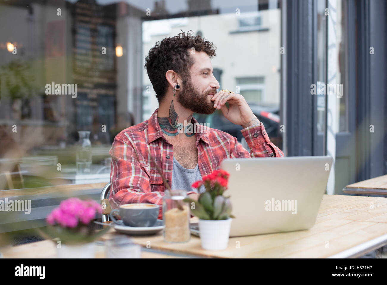 Young tattooed hipster using laptop outside cafe Stock Photo