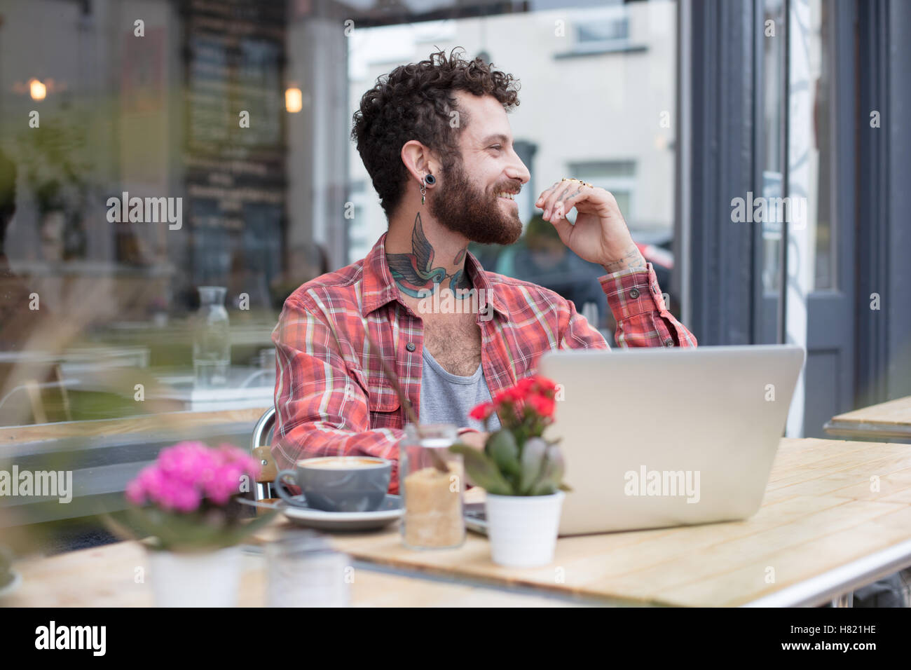 Young tattooed hipster using laptop outside cafe Stock Photo
