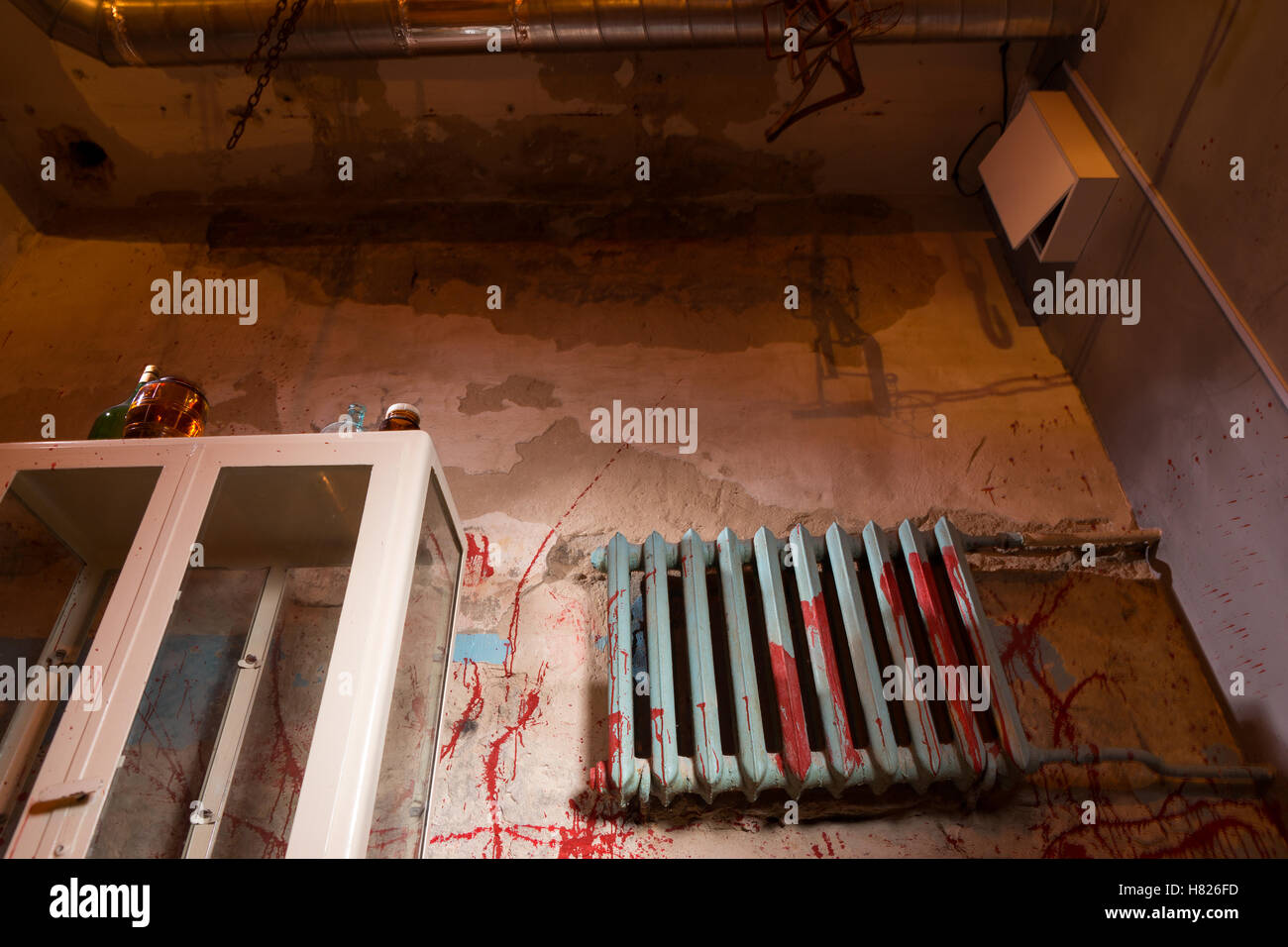 Terrible bloodied battery near glass case in dimly lit basement with pipes  and wires in foreground in a Halloween horror concept Stock Photo - Alamy
