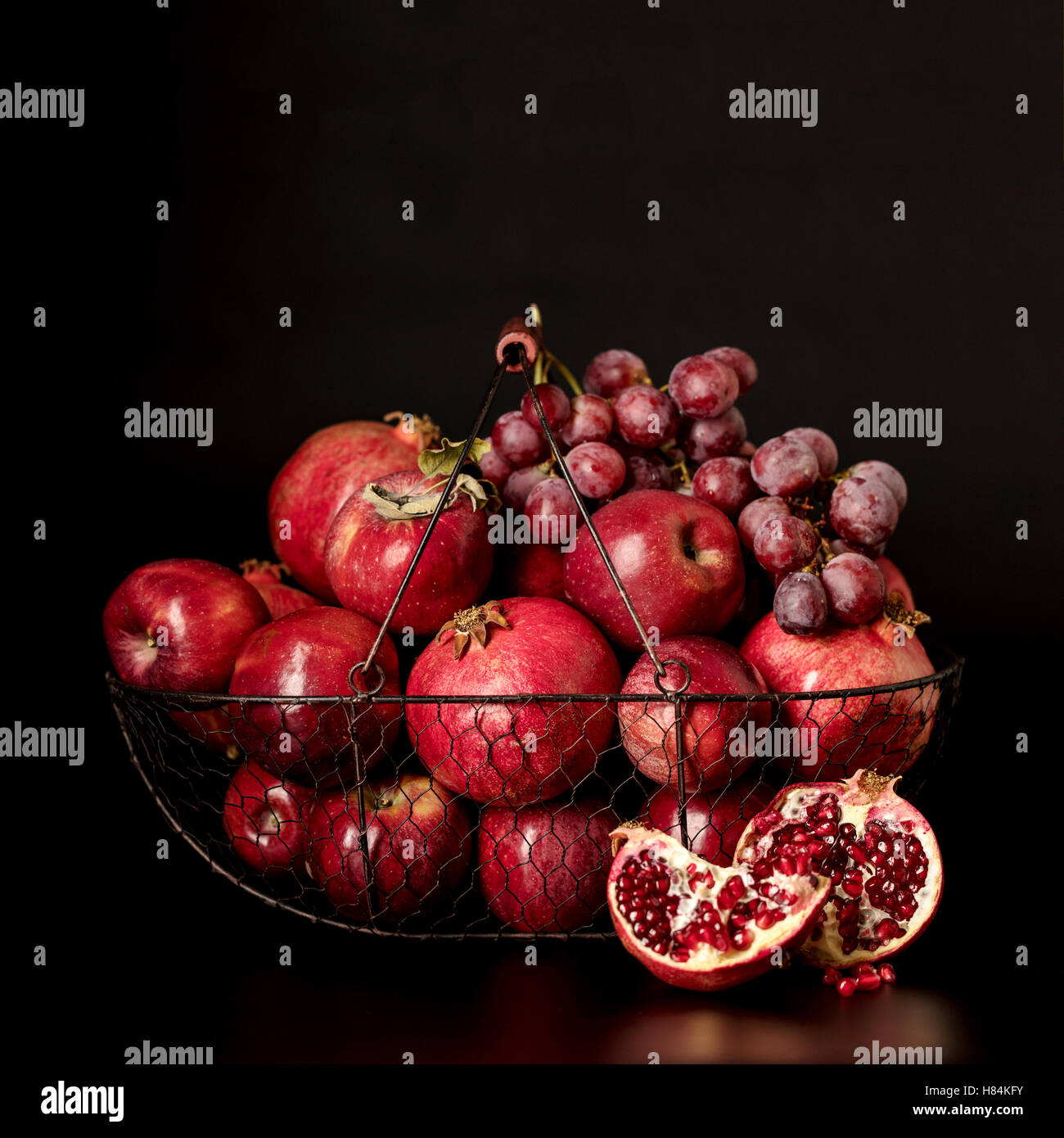 Still life on a dark background. Fruits and berries (apples, pomegranates and grapes) in the basket. Stock Photo