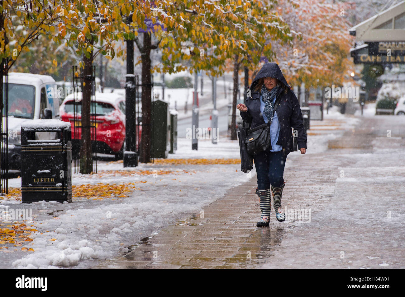 Ilkley, West Yorkshire, UK. 9th November 2016. It is snowing and a lady (wearing boots and a winter coat with hood up) is walking past shops on The Grove - Ilkley's first snowfall of 2016. Credit:  Ian Lamond/Alamy Live News Stock Photo