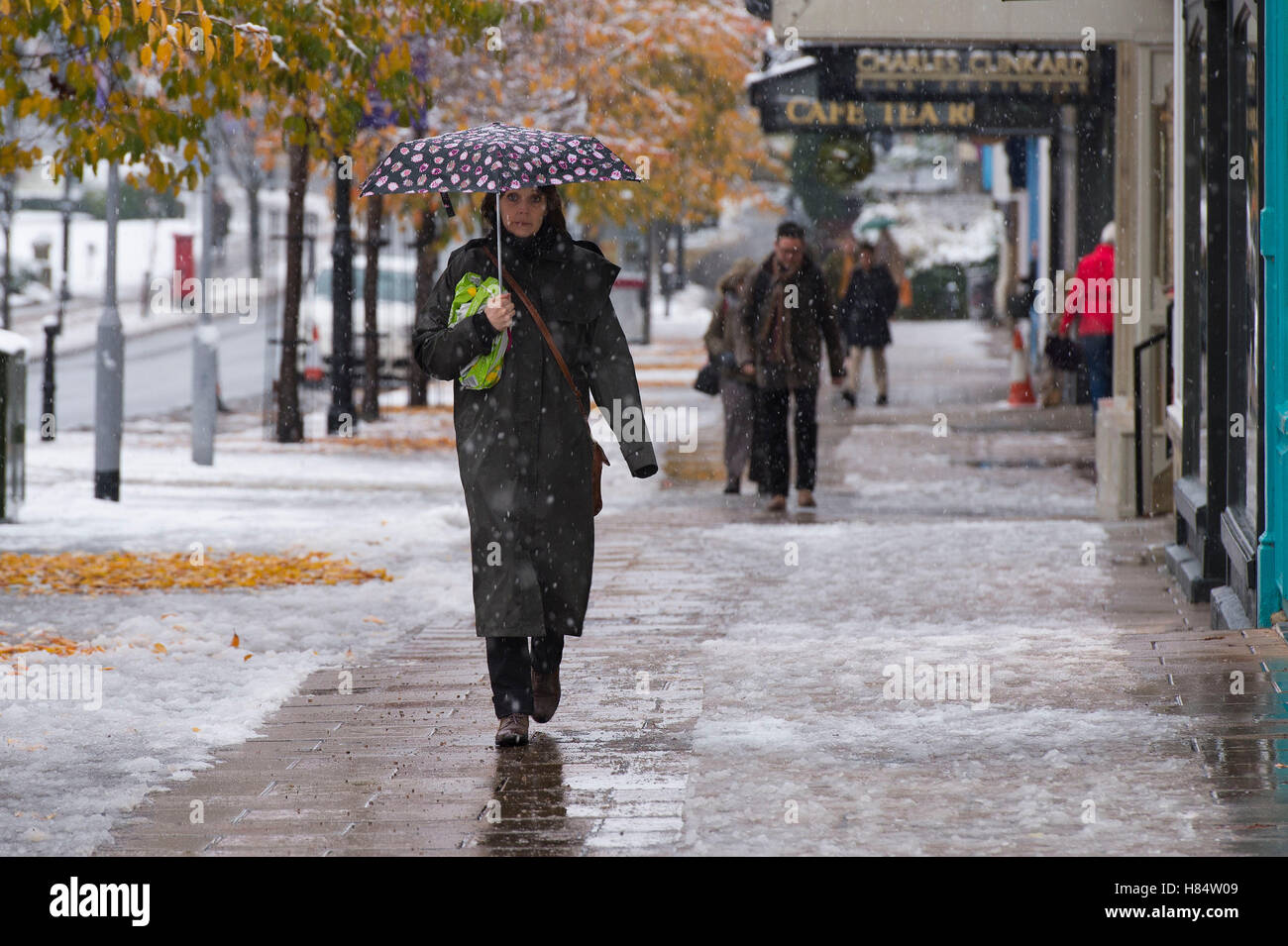 Ilkley, West Yorkshire, UK. 9th November 2016. It is snowing and pedestrians (wearing boots, winter coats and holding umbrellas) are walking past shops on The Grove - Ilkley's first snowfall of 2016. Credit:  Ian Lamond/Alamy Live News Stock Photo