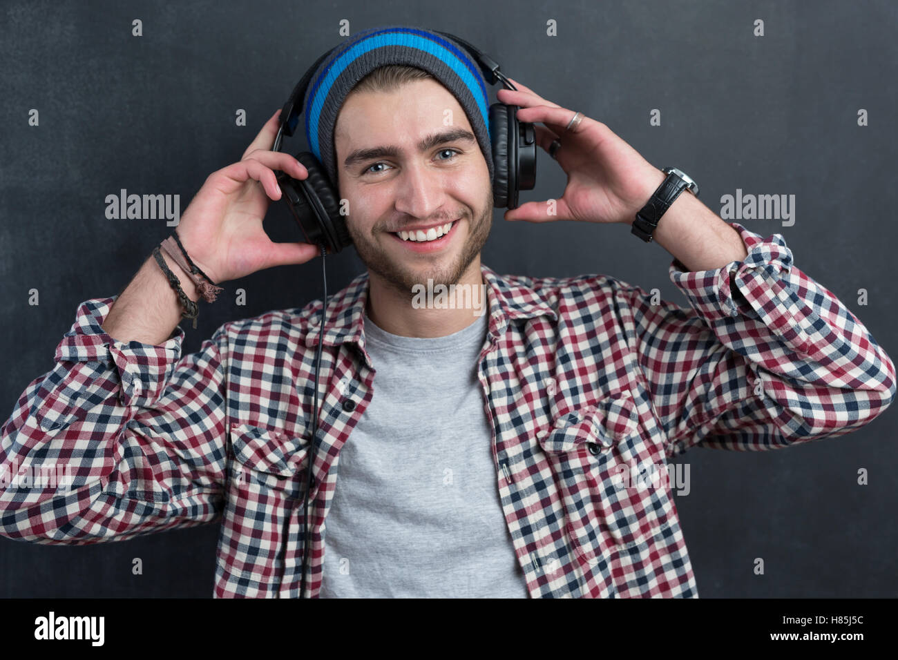 Portrait of confident young DJ with stylish haircut and headphones on dark background Stock