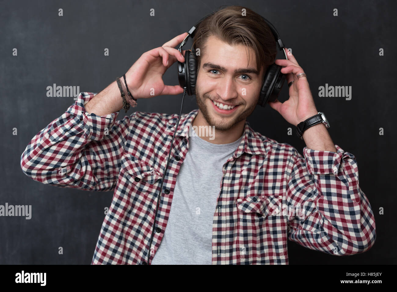 Portrait of confident young DJ with stylish haircut and headphones on dark background Stock