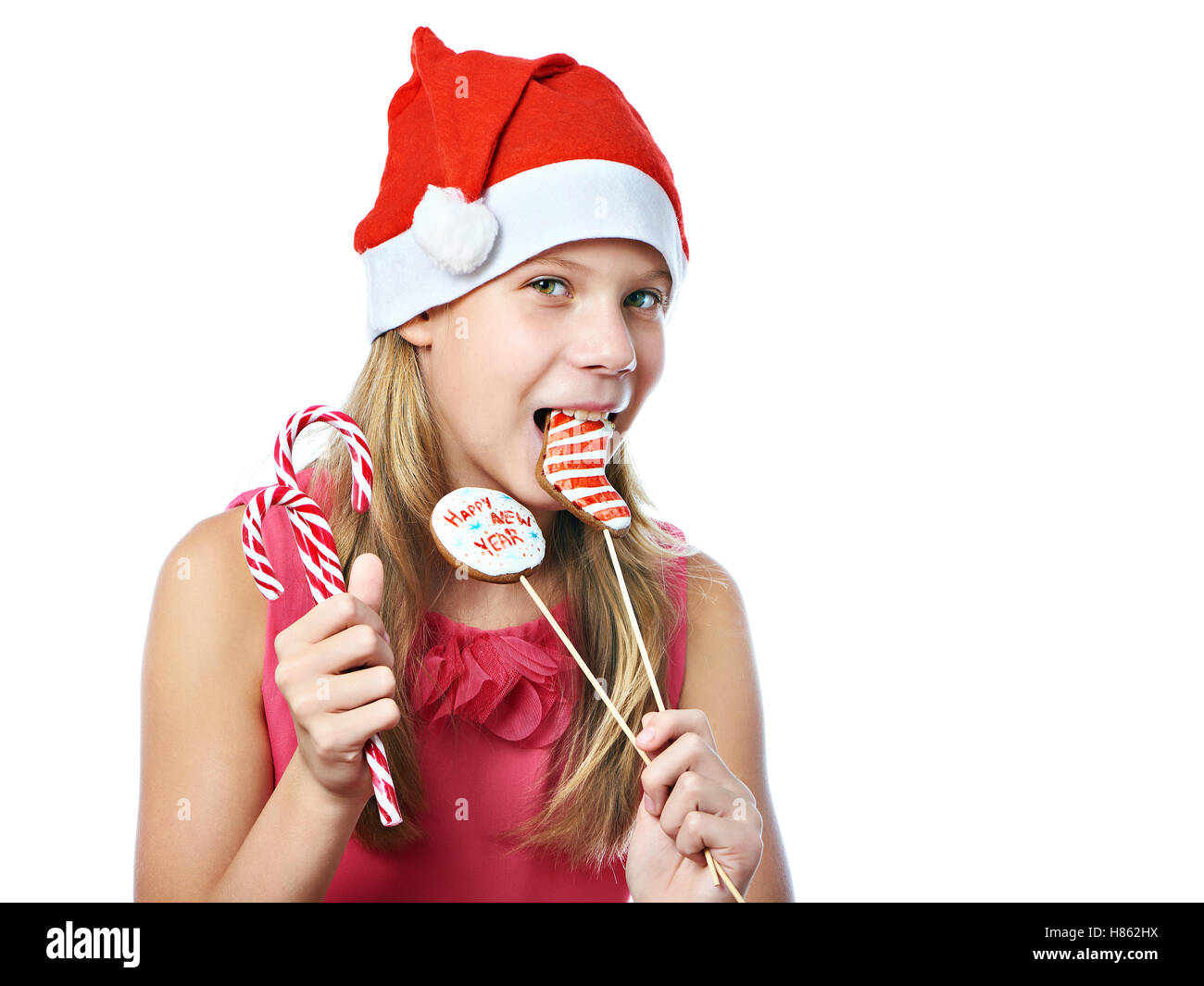 Happy teen girl in red cap eating Christmas cookie isolated white Stock Photo