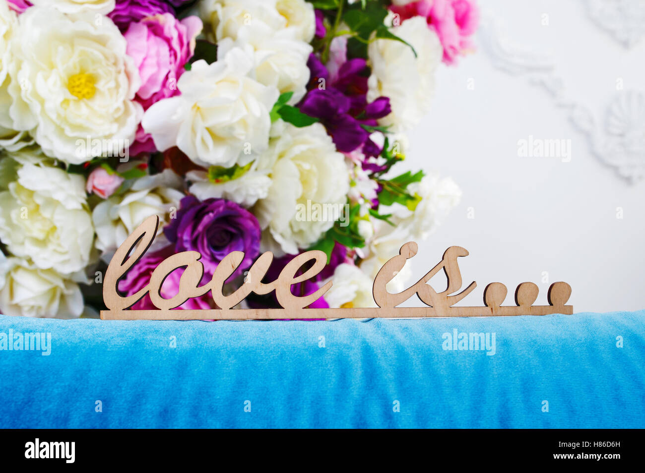 wooden words LOVE IS... against the background of a bouquet flowers Stock Photo