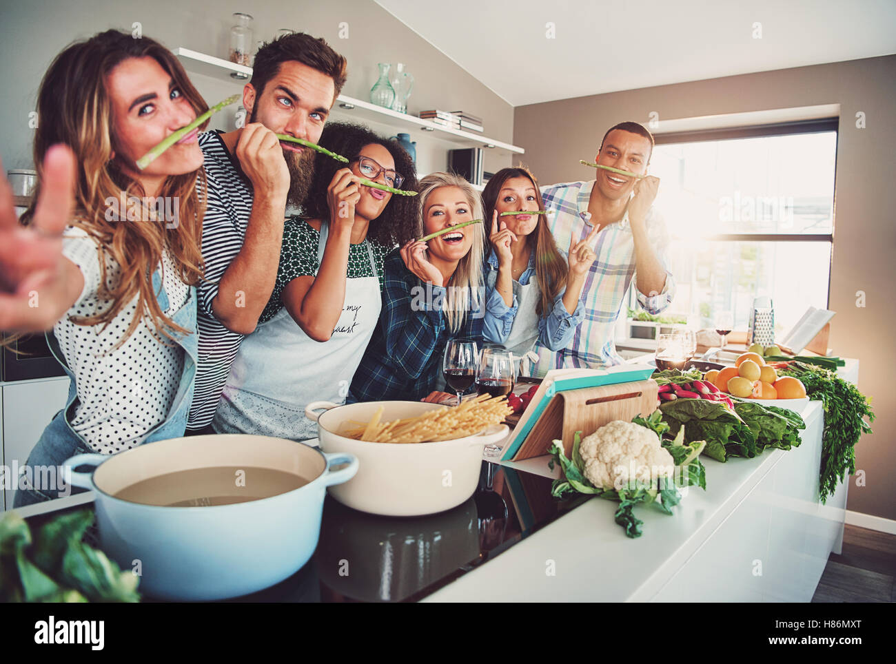 Five friends having a little break to fool around with some asparagus while cooking Stock Photo