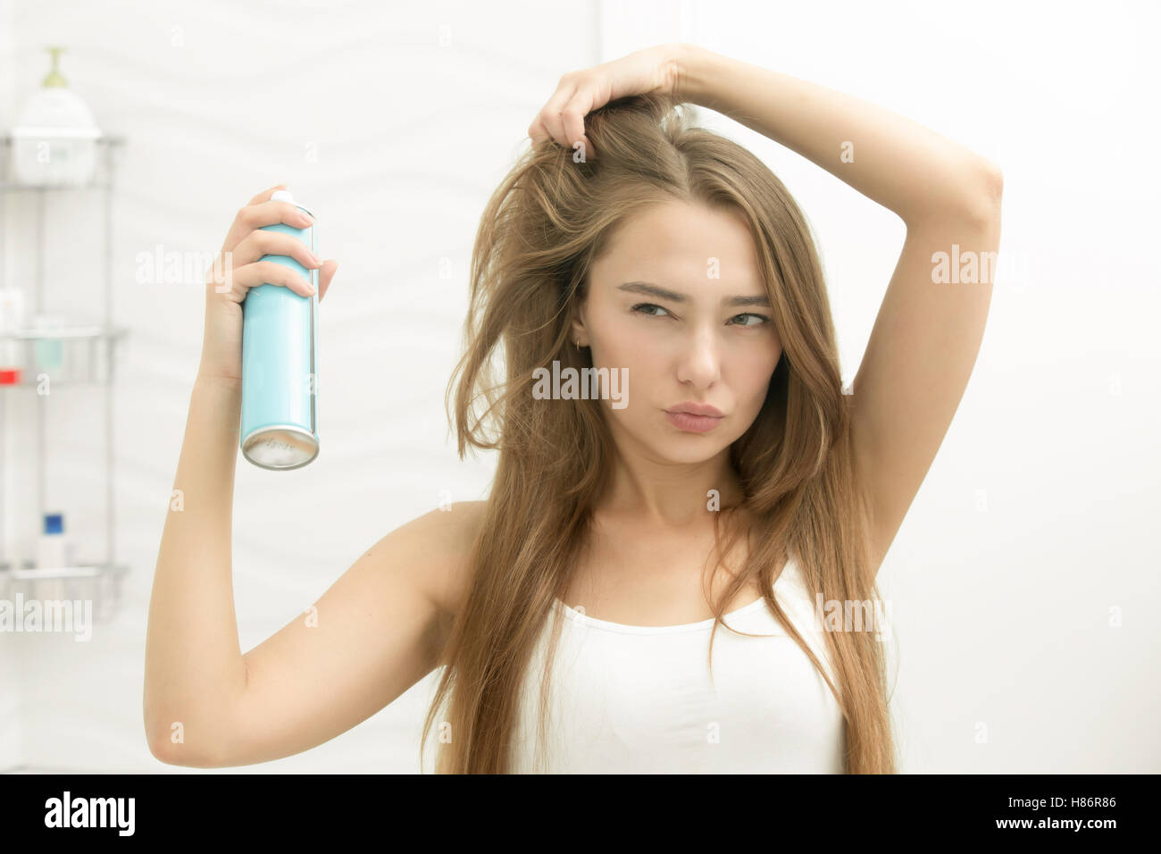 Beautiful young girl applying hair spray on her hair Stock Photo