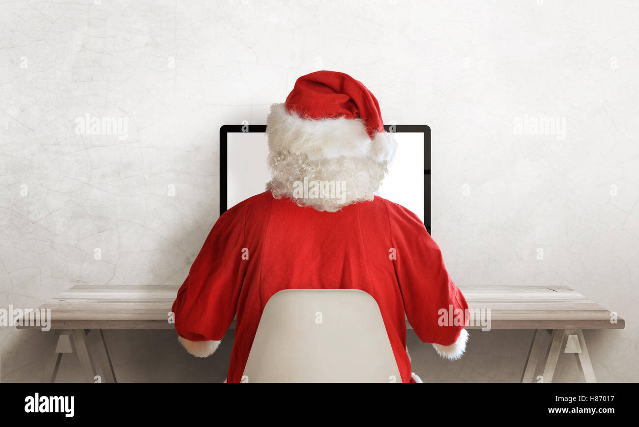 Santa Claus work on computer. View from back. Free space beside from text. Empty work desk. Stock Photo