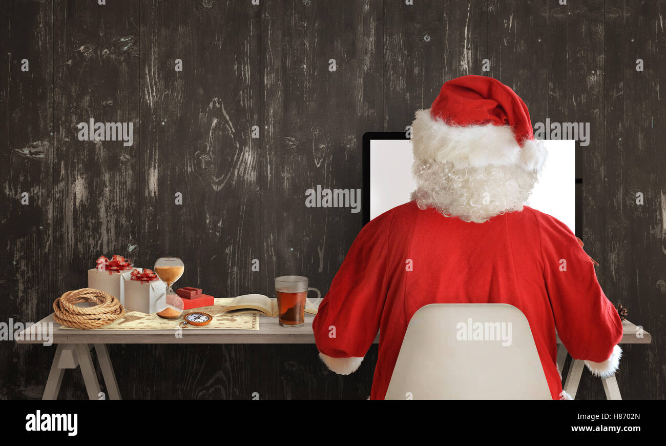 Santa Claus is preparing for a trip and sharing gifts on computer. Beside on table is a map, compass, hourglass, book with instr Stock Photo