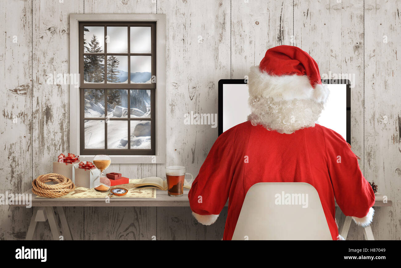 Santa Claus work on computer in his room. White wooden wall with window in background. Stock Photo