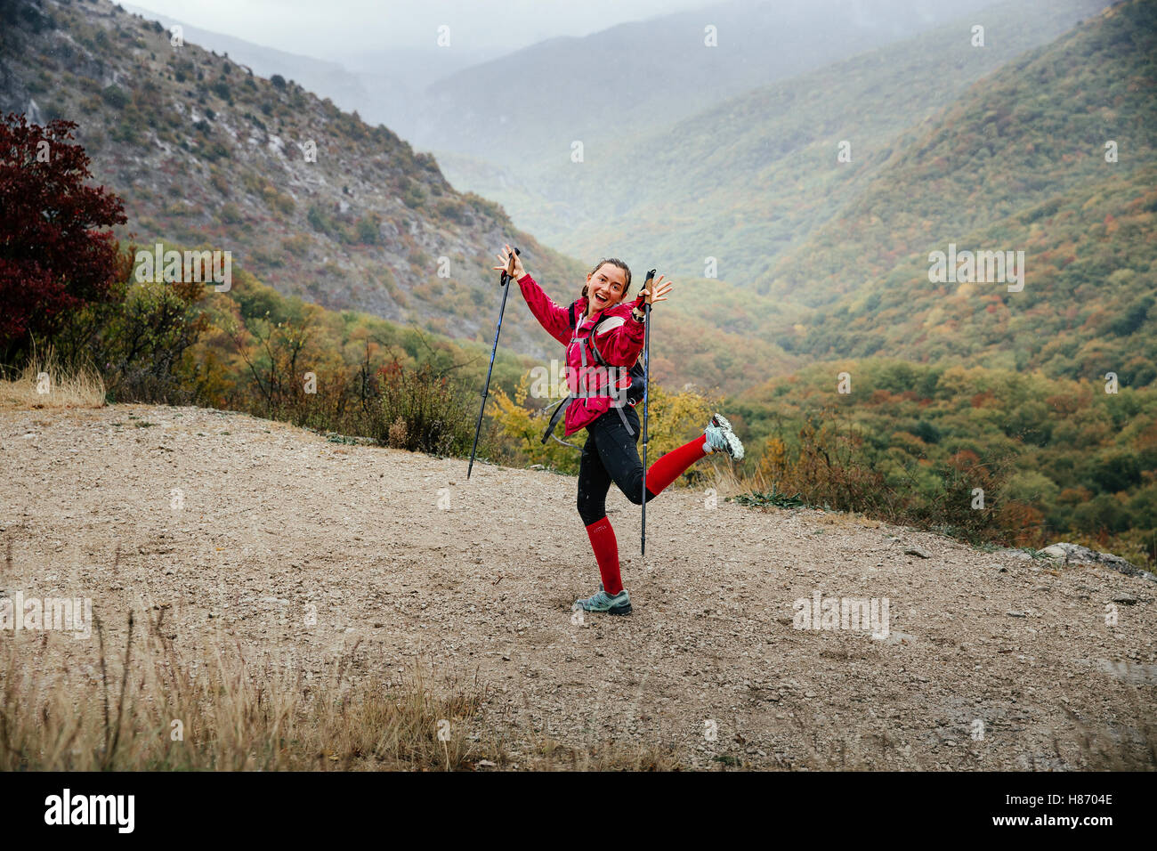 young girl tourist with walking sticks fooling around on a mountain trail in rain during Crimea mountain marathon Stock Photo