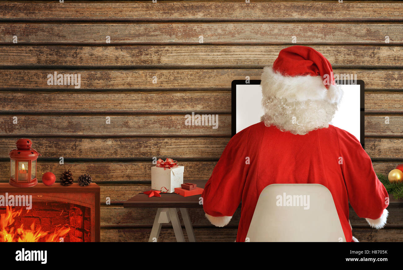 Santa Claus shopping online on computer from his warm room. In addition to the fireplace with fire Stock Photo