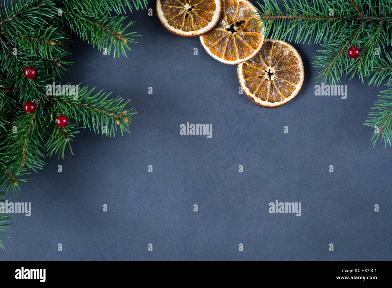 Background for Christmas or New Year: fir tree, cranberries and dry oranges over dark background. Copy space for text. Mock up Stock Photo