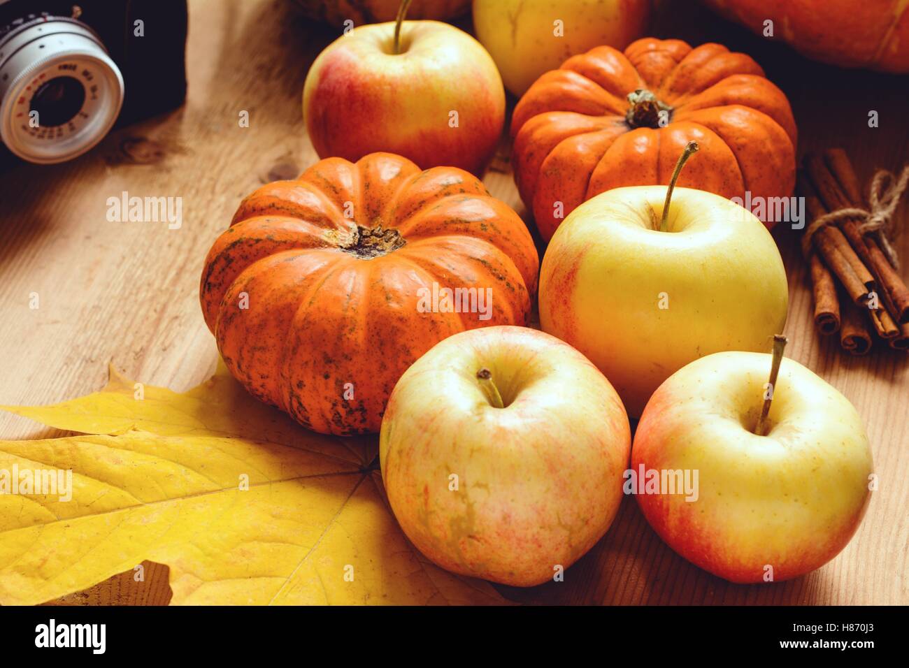 Autumn still life with retro camera, pumpkins, apples, fallen leaves and cinnamon sticks. Warm tones Stock Photo