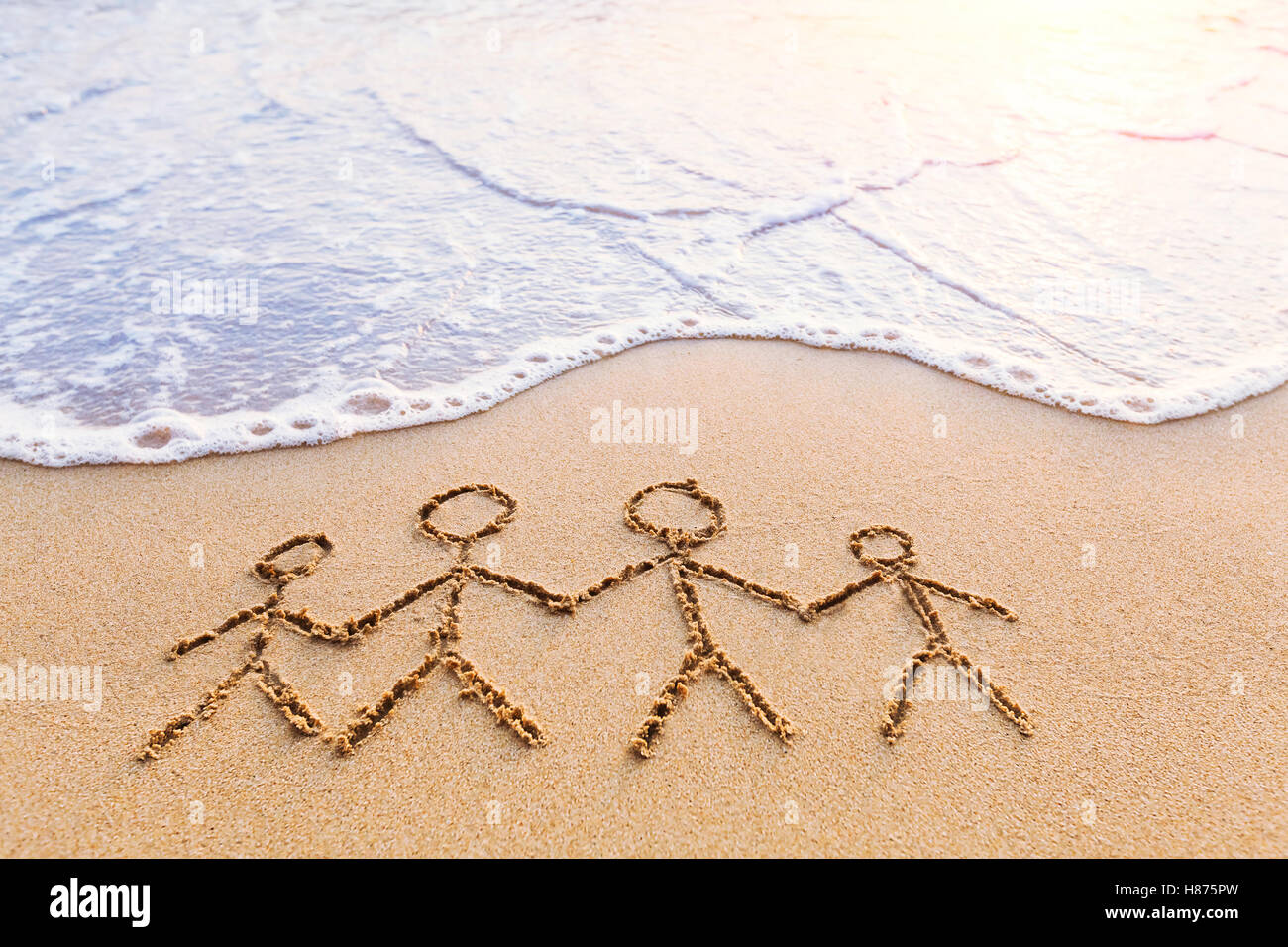 Symbol of happy family with parents and children holding hands together drawn in the sand near the sea - concept united people Stock Photo