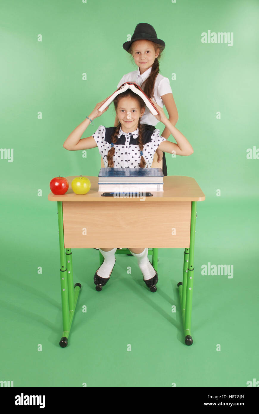 Two girl in a school uniform sitting at a desk and reading a book ...