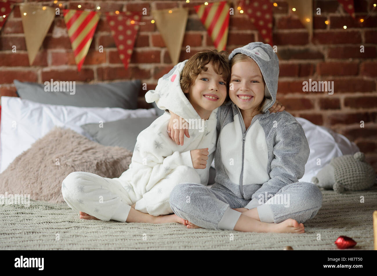 Christmas. Two children in pajamas sitting on the bed waiting for Christmas gifts. The bedroom is decorated with festive garland Stock Photo