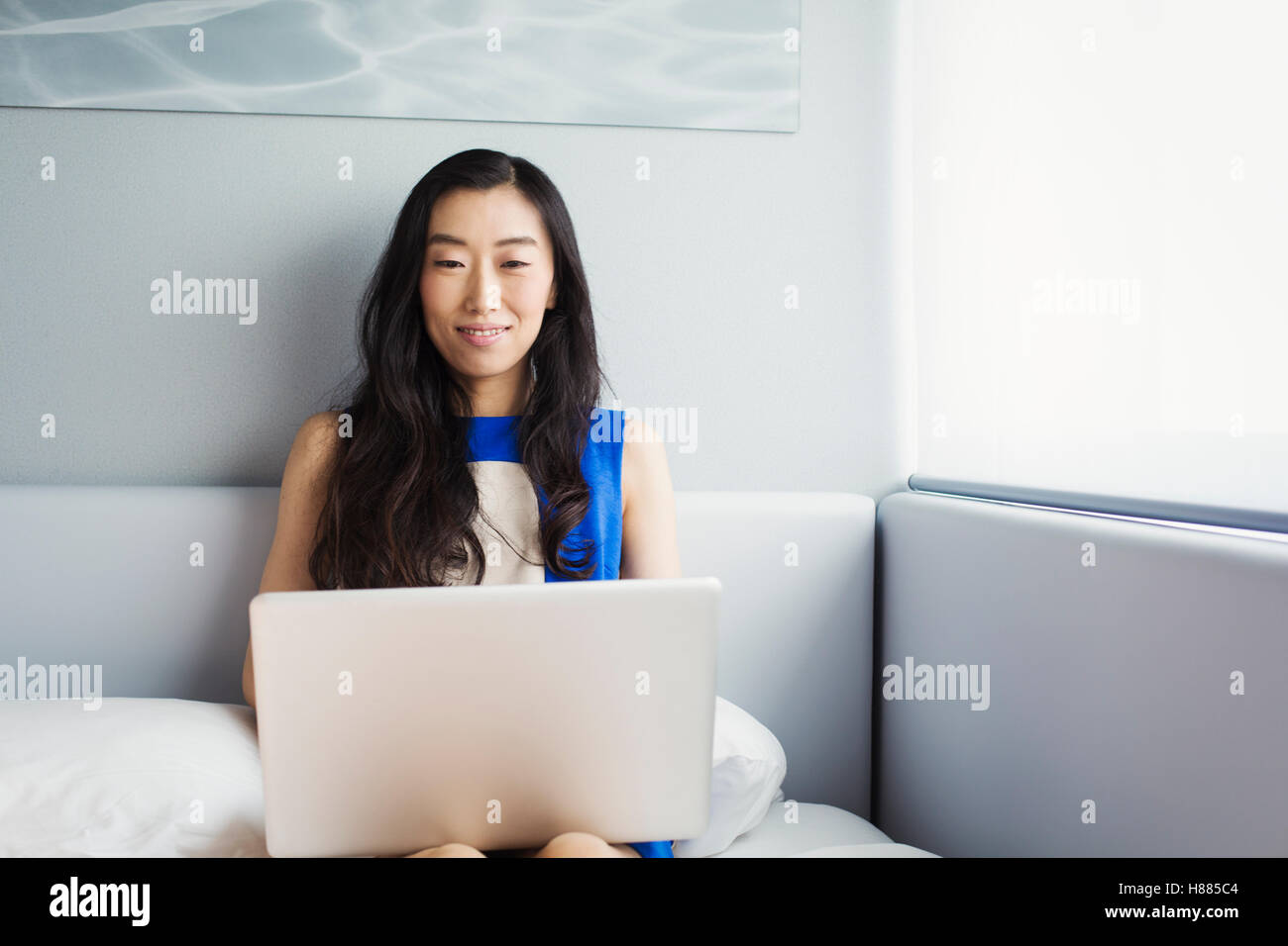 A business woman preparing for work, sitting on a bed using her laptop computer. Stock Photo