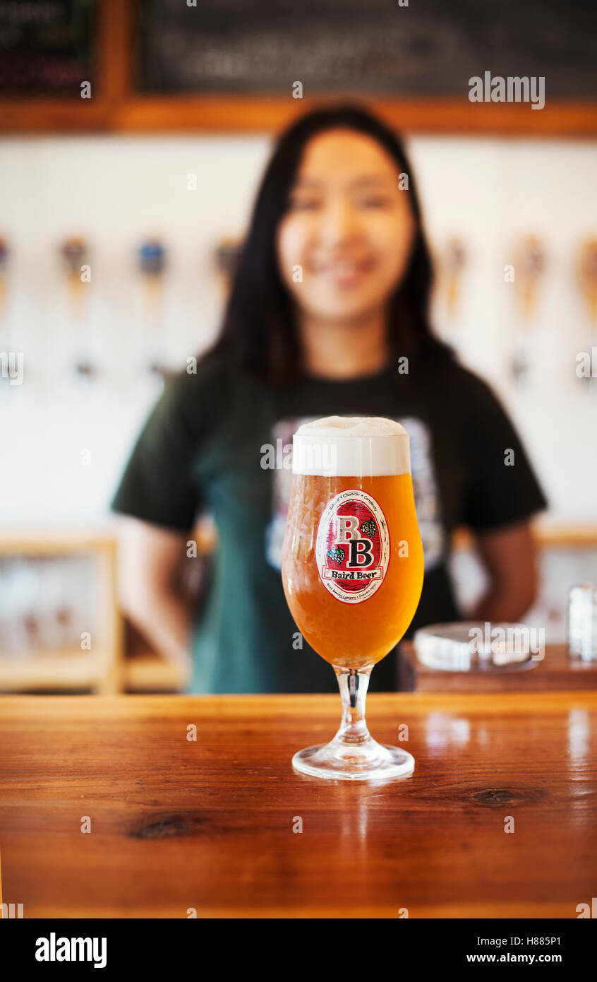 Beer glass standing on a counter, woman in the background. Stock Photo