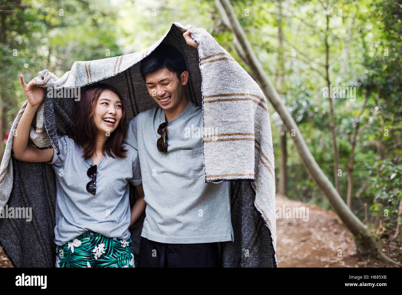 Young woman and man standing in a forest, holding a blanket over their
