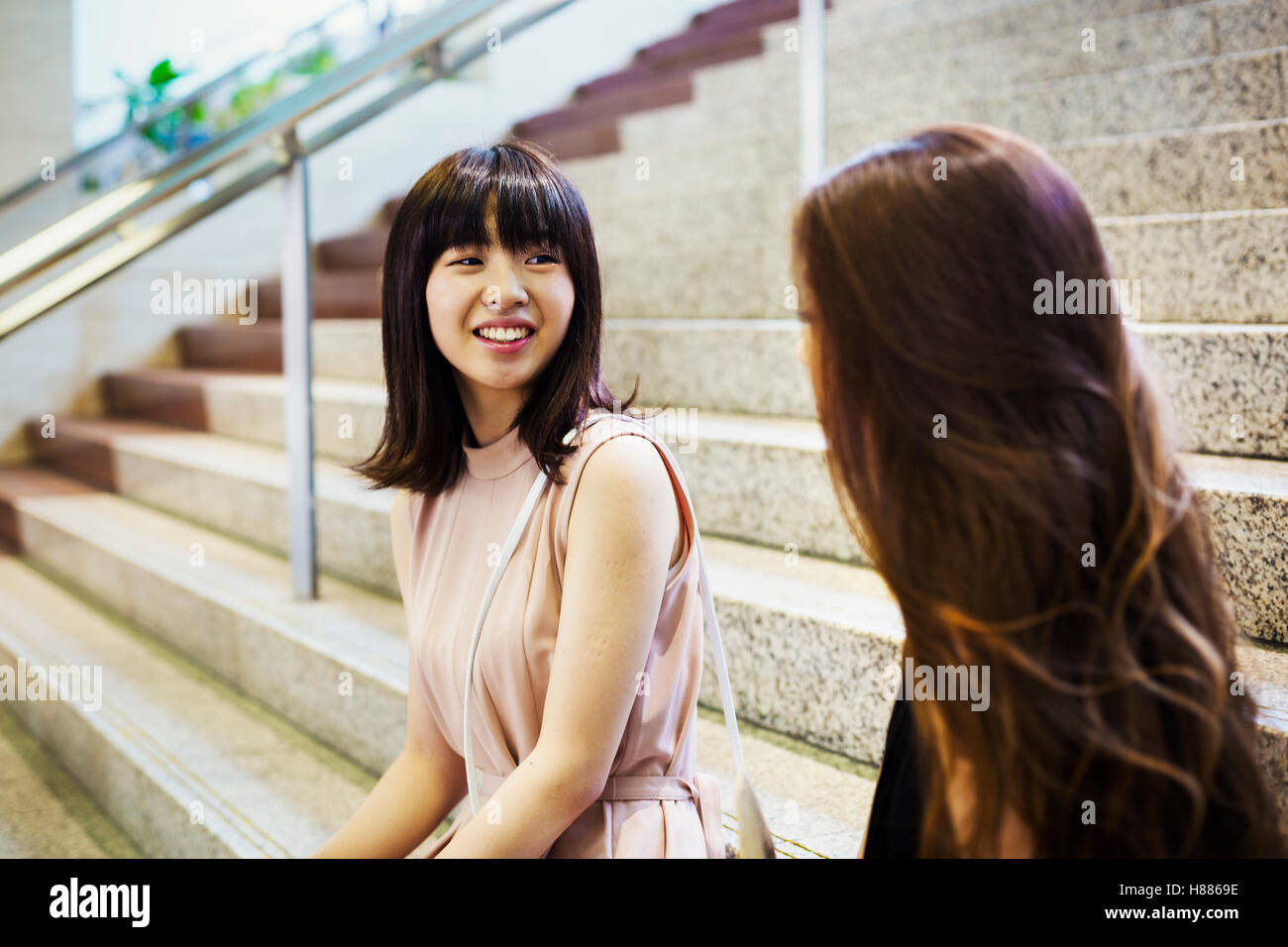 Two smiling young women with long brown hair sitting on a staircase. Stock Photo