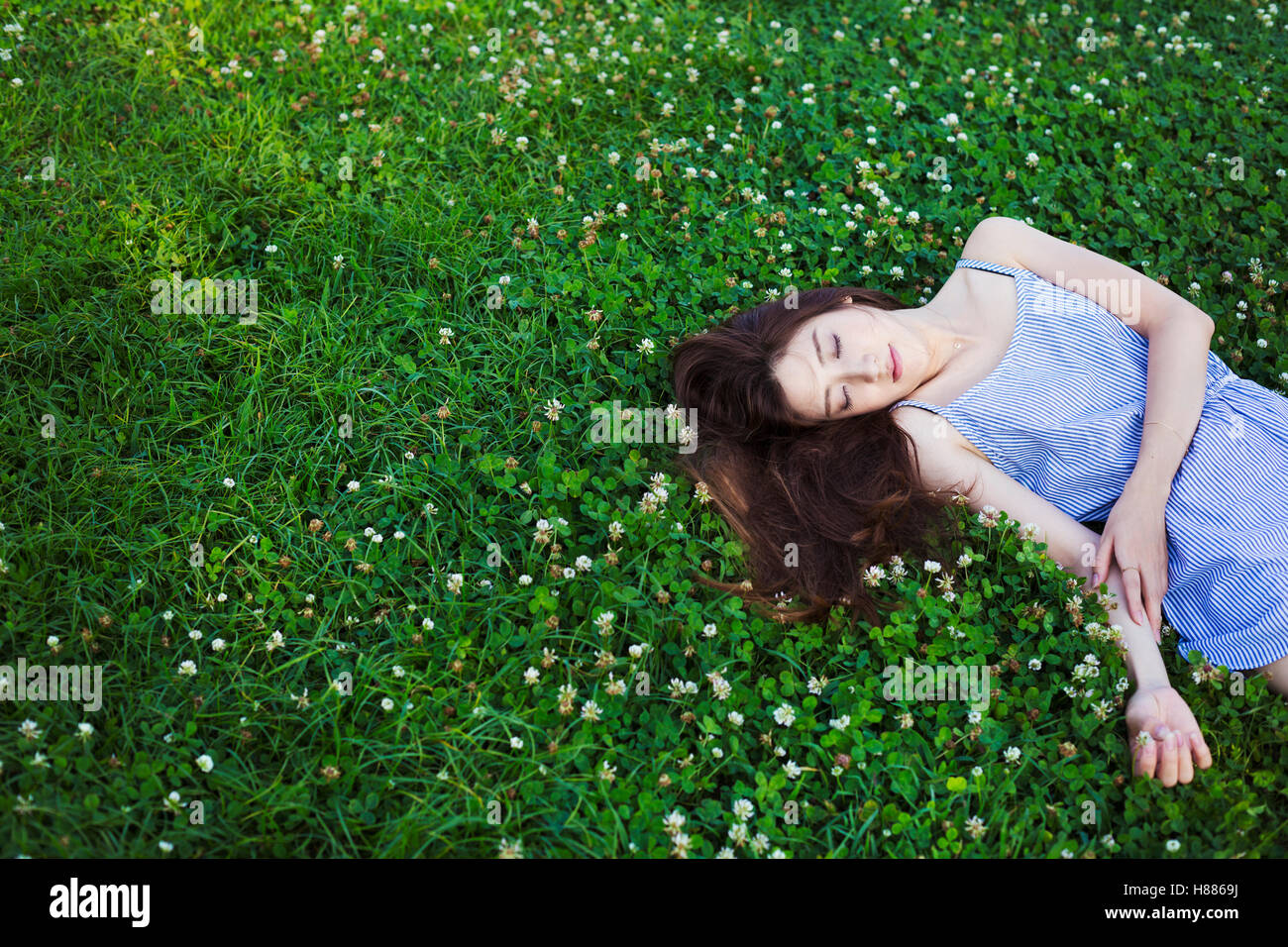 Young woman with long brown hair lying on a lawn. Stock Photo