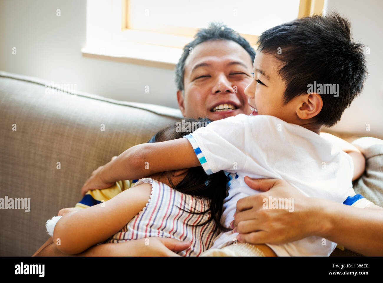Family home. A man cuddling his daughter and son on a sofa. Stock Photo