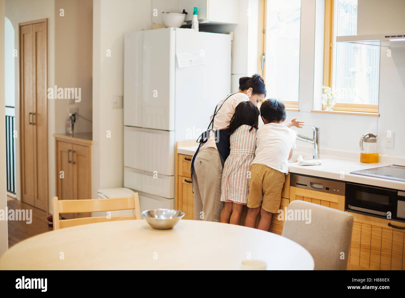 Family home. A mother and two children standing at the sink in a kitchen. Stock Photo