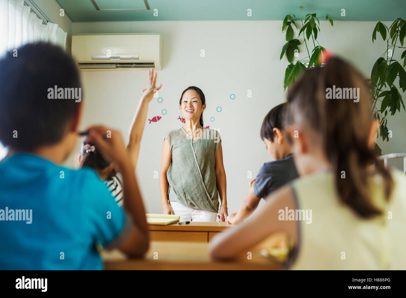 A group of children in a classroom, one with her hand up ready to answer a question. Stock Photo
