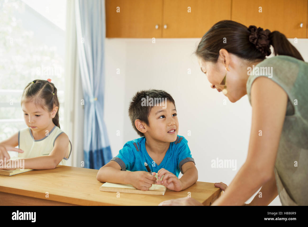 A teacher talking to two children sitting at a desk. Stock Photo